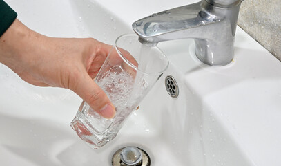 Close up of filling glass with water from sink faucet in bathroom