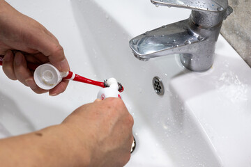 Squeezing toothpaste onto toothbrush at bathroom sink, daily oral hygiene routine