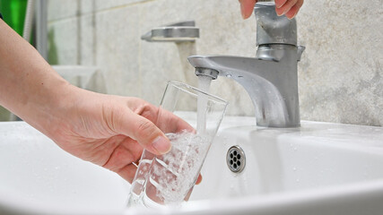 Close up of filling glass with water from sink faucet in bathroom