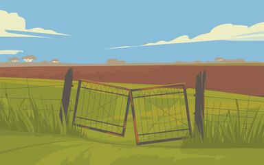 A fallen soccer goal lies in a grassy field near a fence under a blue sky with clouds.