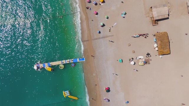 Oludeniz, Turkey. Aerial top down view of Oludeniz Beach with rows of umbrellas, crowded pebble shore, sea waves and pontoon pier in turquoise water, summer. Aerial View, HEAD OVER SHOT, HEAD OVER SH