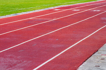 Fototapeta premium Red running track with lanes 3 to 5 marked in white, bordered by grass and concrete, ideal for race visuals.