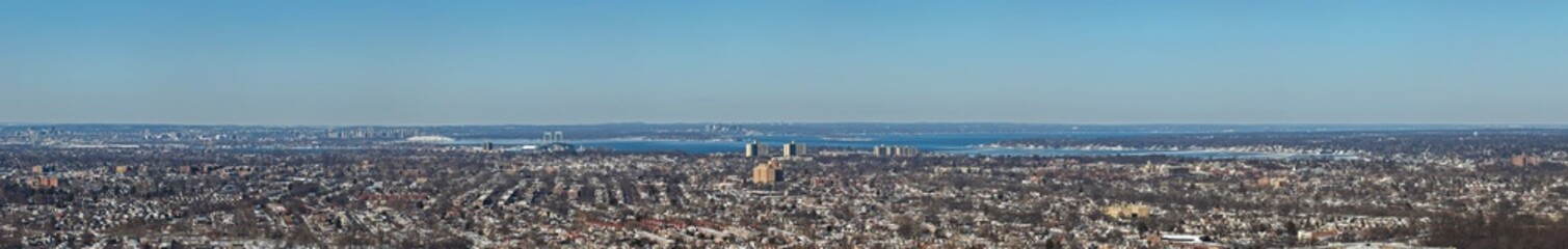 Obraz premium Fresh meadows queens cityscape unfolding across a vast urban landscape toward a distant body of water and lower manhattan skyline, capturing a wide perspective on a clear winter day