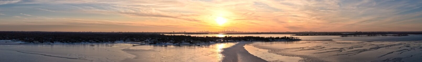 Naklejka premium Panoramic winter sunset painting the long island sound with warm colors, reflecting on the partially frozen water near plum beach point in port washington, new york