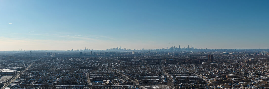 Aerial panoramic view showing fresh meadows, queens, covered in a light snow, with the iconic manhattan skyline visible in the distance under a clear blue sky