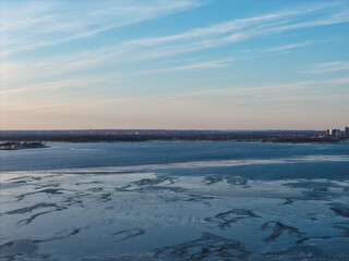Obraz premium Manhasset bay, port washington, ny, with vast ice floes drifting across cold blue water toward a distant shoreline and urban silhouette beneath a pale winter sky