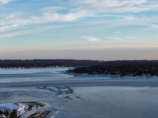 Cold winter landscape showing a partially frozen bay, with ice floes and broken ice covering the water near the snow dusted shoreline and houses, under a light blue sky in port washington, new york
