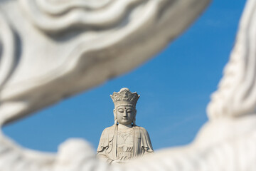 Obraz premium White Buddha statue framed by soft foreground sculpture against blue sky