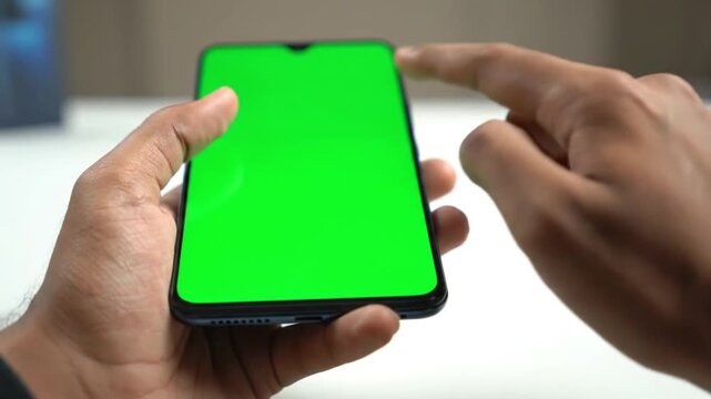 close up of person holding smartphone with green screen chroma key display for mobile app design mockup and digital interface presentation on blurred office background