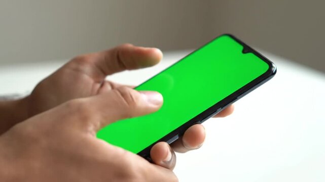 male hands holding modern smartphone with green screen chroma key display in horizontal position for mobile app interface design mockup and digital media content presentation