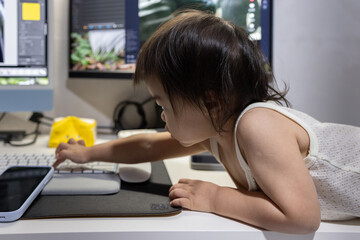 A toddler explores a home office, reaching for the keyboard.