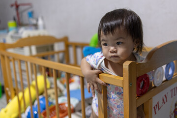 Cute baby girl holding crib railing while looking forward