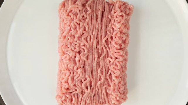 Fresh uncooked minced turkey meat rotating on a white plate, isolated on a white background.