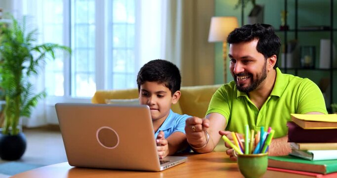 Indian asian kid cracks online exam on laptop while father rejoices sitting beside him at desk during digital test result celebration in cozy modern home interior