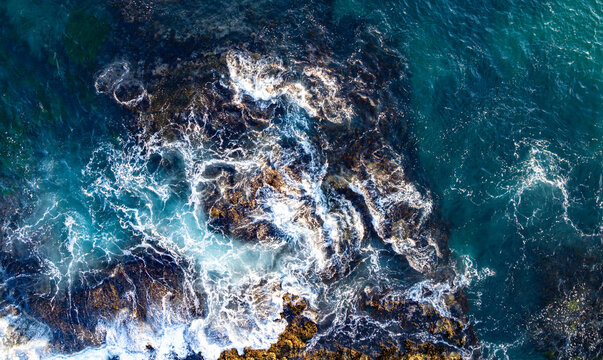Turquoise water with reef. Blue ocean water. Coastline from above. Summer beach with crashing waves. Dramatic coastline. Ocean surface. Rocky coast with sea foam. Wave moving.