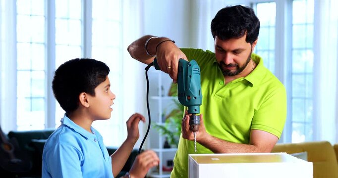 Indian father teaches son assembling furniture using drilling machine while working hands on with wooden tools at home as child observes learning practical life skills in modern indoor living space