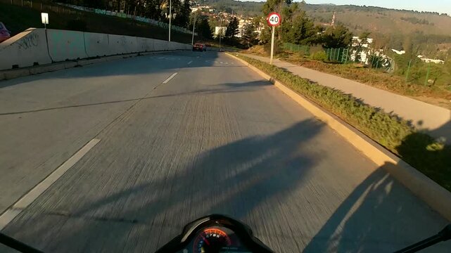 First-person POV motorcycle ride along an urban road, showing lane markings, traffic ahead, and surrounding city landscape in daylight with smooth forward motion.