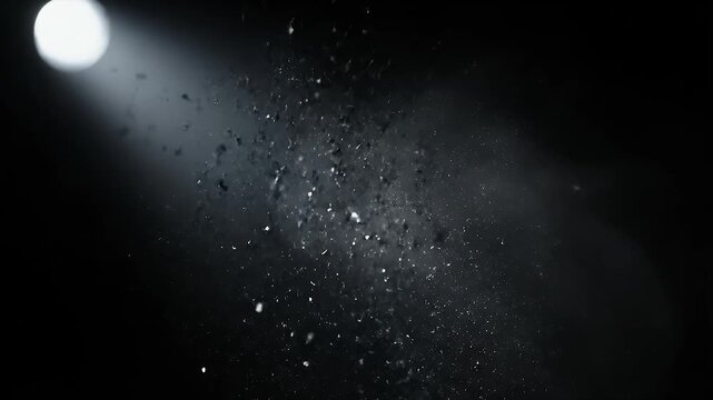 A static close-up shot of shimmering black carbon dust and soot particles dancing in a single dramatic beam of light in a dark room.