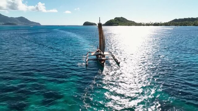 A traditional outrigger sailing across the ocean in a bright, sunny day. Island is in the background