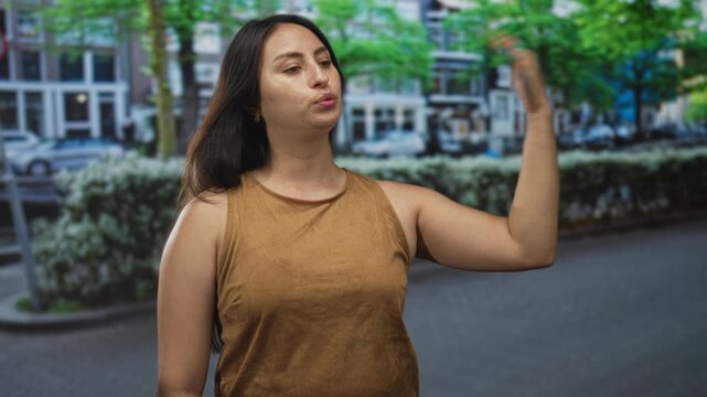 Woman hand to forehead on street in front of row houses and hedges, lips pursed gesture wearing brown sleeveless top; annoyance.