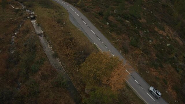 High-speed FPV drone footage of a sporty car driving aggressively over the Col des Montets mountain pass near Chamonix during autumn with colorful foliage fast cornering and dynamic alpine road action