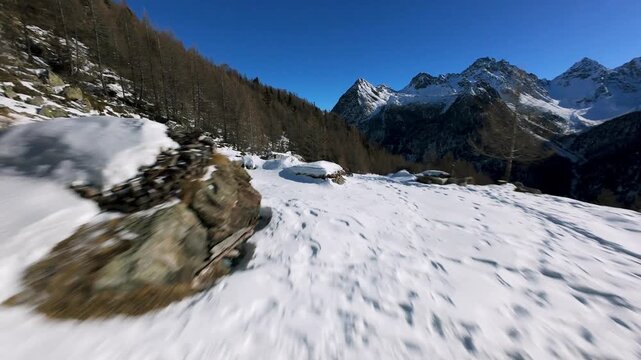 Dynamic FPV drone footage flying over traditional stone mountain huts covered in deep snow in Alpe dell Oro, Valmalenco, Italian Alps