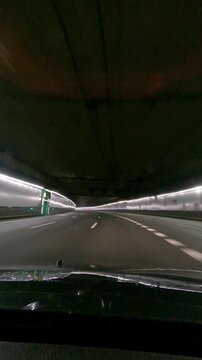 Vertical hyperlapse POV from inside a vehicle driving at night through illuminated M30 tunnels in Madrid during rain, entering near Casa de Campo and exiting toward A3 under M40 highway.