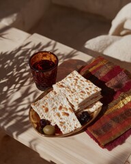 Jewish Matzah Bread on a Golden Plate with Wine Glass and Olives for Passover Seder Meal Arrangement on Wooden Table with Natural Leaf Shadows for Holiday Branding