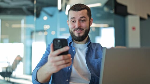 Positive emotions radiate as man views smartphone. Surprise and happiness evident from good news. Modern office setting promotes focus and digital connection.