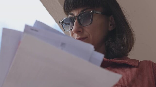 A woman stands near a mailbox, looking at letters. A woman in glasses stands on a city street, concentrating on holding papers and envelopes. A girl receives mail. 
