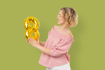 Fototapeta premium Woman holds gold balloon shaped like number 8 and smiles