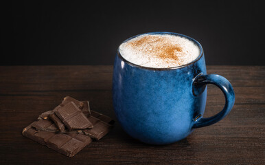 A cup of delicious, aromatic coffee with chocolate pieces on a dark background