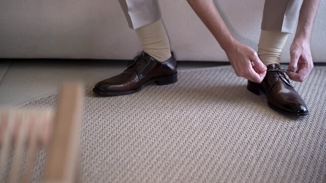 A person sits down in a living room and puts on dark shoes. They adjust their light-colored socks and make sure everything fits well. This shows a moment of getting ready.