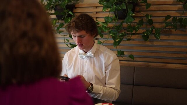 Guy checks his phone at the cafe while a message from another girl appears during the date creating quiet tension as he avoids eye contact and the moment turns uncomfortable