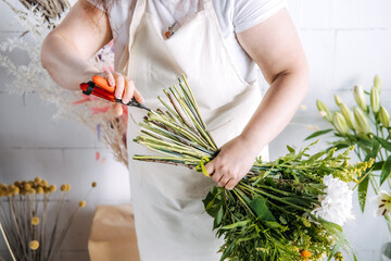 Florist uses hand pruners to trim stems of large mixed flower bouquet in studio. Fresh cut flowers, greenhouse-to-market, sustainable supply chain.