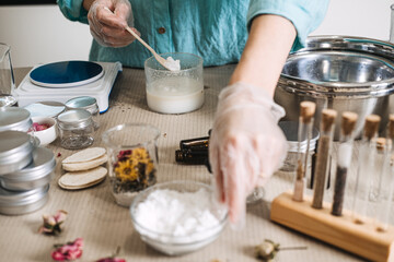 Hands in gloves reach for ingredients while mixing white powder into beaker among jars of dried flowers. botanical extracts, raw beauty ingredients, herbal apothecary, natural formulation art.