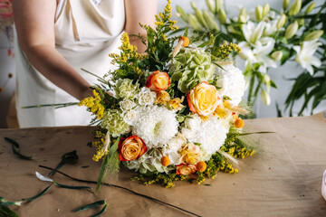 Artisan at work assembles floral bouquet with roses and hydrangeas during flower workshop. Handmade floral arrangement, flower workshop, artisan at work.