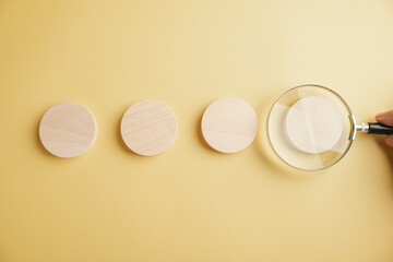 Three wooden circles on a yellow background, one magnified by a magnifying glass.