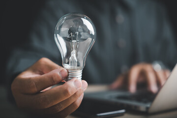 Closeup of a man hand pose with a sign gesture holding a lightbulb, a clear sign of creative ideas and innovation for business solutions while working on a laptop at the desk