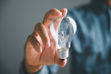 A hand holds a lit light bulb, symbolizing ideas and innovation.  The background is blurred,...