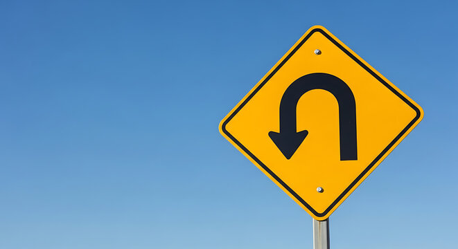 A curved arrow sign indicates a sharp turn ahead on a clear day against a blue sky viewed from a straight road