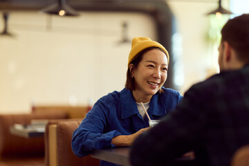 Asian Woman In Yellow Beanie Enjoying Friendly Conversation At Diner Cafe Table