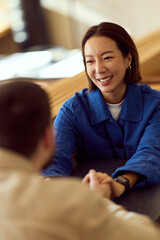 Asian Woman In Blue Shirt Smiling While Shaking Hands Across Table At Diner