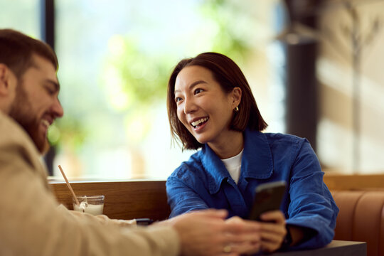 Asian Woman in Blue Shirt Laughing With Friend at Diner During Casual Conversation