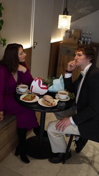 Vertical screen guy struggles to hide his feelings during the date realizing the girl is not the right match while they sit in a calm cafe atmosphere with pastries and tea between them