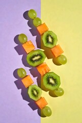 Vertical pattern of fresh fruit on wooden skewers, healthy kiwi and grape snacks on purple and yellow background, candid lifestyle food illustration