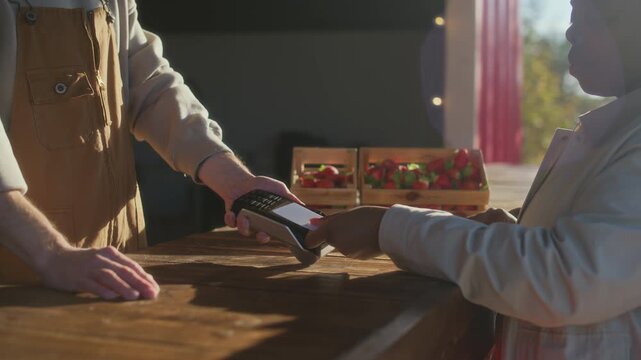 Slowmo closeup of unrecognizable customer using credit card while paying for fresh farm strawberry being sold at outdoor market stall on sunny day