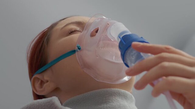 A woman inhales steam from a nebulizer filled with saline solution. She wears a mask on her face to treat her cough and manage respiratory infections.