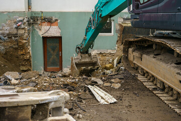 Fototapeta premium Heavy excavator operating near building foundation during renovation work, construction machinery, demolition process and urban infrastructure repair.