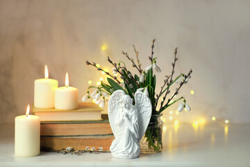 Fototapeta premium praying angel figurine, burning candles, books, snowdrop flowers and willow in vase on table. Easter, Palm Sunday holidays concept. Christian church fest. symbol of faith in God, Lent, religion